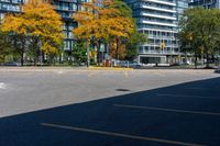 a bus stop sign in a parking lot near a tall building with trees and cars