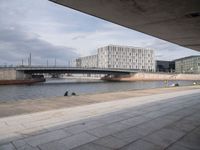 an empty concrete road on a bridge near buildings and the river in front of it