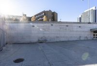 the shadows are cast from a building with high rise buildings in the background at a bus stop