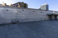 the shadows are cast from a building with high rise buildings in the background at a bus stop