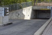 a concrete ramp is attached to a gray concrete wall under a bridge with a sign warning pedestrians on it