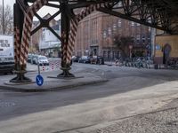 cars and a bike pass under a road with pedestrian traffic at an intersection near a building with tall buildings