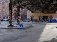 cars and a bike pass under a road with pedestrian traffic at an intersection near a building with tall buildings