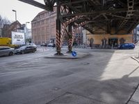 cars and a bike pass under a road with pedestrian traffic at an intersection near a building with tall buildings