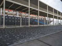 a train station with some cars parked outside of it by a fence and cobblestone walkway