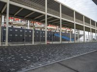 a train station with some cars parked outside of it by a fence and cobblestone walkway