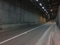 an empty road in a tunnel with lights on and concrete walls on either side of the wall