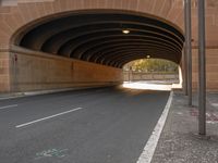 a long tunnel is near the street with several cars coming in and going around it