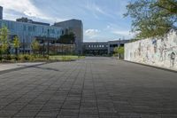 a walkway and sidewalk near buildings with graffiti on them and trees and shrubs in the foreground