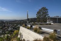 a long cement bench on top of a hill next to a fence and trees in a city area