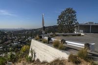 a long cement bench on top of a hill next to a fence and trees in a city area