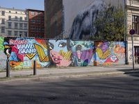 street wall with some murals on it and several buildings next to it with people walking