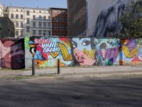 street wall with some murals on it and several buildings next to it with people walking