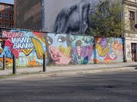 street wall with some murals on it and several buildings next to it with people walking