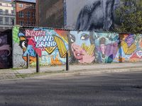 street wall with some murals on it and several buildings next to it with people walking