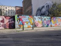 street wall with some murals on it and several buildings next to it with people walking