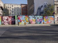 street wall with some murals on it and several buildings next to it with people walking