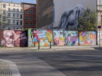 street wall with some murals on it and several buildings next to it with people walking