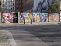 street wall with some murals on it and several buildings next to it with people walking