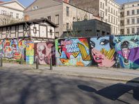 street wall with some murals on it and several buildings next to it with people walking