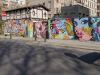 street wall with some murals on it and several buildings next to it with people walking