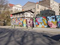 street wall with some murals on it and several buildings next to it with people walking