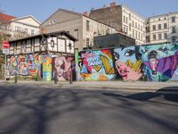 street wall with some murals on it and several buildings next to it with people walking