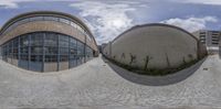 two spherical photographs are shown in the middle of a walkway, with a circular object on the right and some buildings on the left