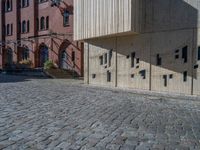 cobblestone driveway surrounded by modern buildings on sunny day with sun reflecting onto the windows