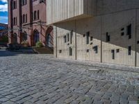 cobblestone driveway surrounded by modern buildings on sunny day with sun reflecting onto the windows