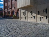 cobblestone driveway surrounded by modern buildings on sunny day with sun reflecting onto the windows