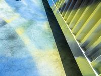 a person walking down an empty street next to yellow blinds and green metal fence with blue sky in the background