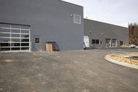 the side of a gray warehouse with glass doors in front of it, in a parking lot