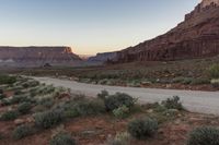 the desert is covered with dirt, bushes and trees at sunset in the distance is the rocky landscape and cliffs