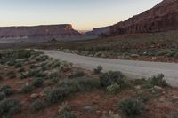 the desert is covered with dirt, bushes and trees at sunset in the distance is the rocky landscape and cliffs