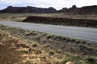 the view looking down the road from a hill at an arid area with grass, rocks and mountains