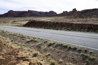 the view looking down the road from a hill at an arid area with grass, rocks and mountains