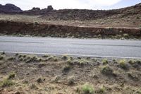 the view looking down the road from a hill at an arid area with grass, rocks and mountains