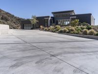 the driveway and garages of the modern house overlook the surrounding mountains and hills in california's malibu valley