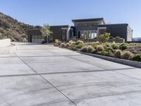 the driveway and garages of the modern house overlook the surrounding mountains and hills in california's malibu valley