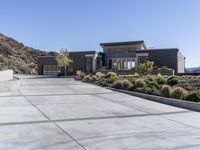 the driveway and garages of the modern house overlook the surrounding mountains and hills in california's malibu valley