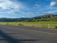 a lone country road is in the countryside area with mountains on both sides and barbed fence between the two sides