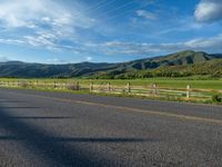 a lone country road is in the countryside area with mountains on both sides and barbed fence between the two sides