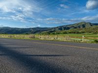 a lone country road is in the countryside area with mountains on both sides and barbed fence between the two sides