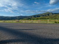 a lone country road is in the countryside area with mountains on both sides and barbed fence between the two sides