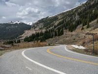 a mountain side with a road running next to the mountains, a bike parked in front of it and trees on one side