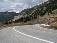 a mountain side with a road running next to the mountains, a bike parked in front of it and trees on one side