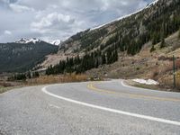 a mountain side with a road running next to the mountains, a bike parked in front of it and trees on one side