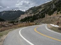 a mountain side with a road running next to the mountains, a bike parked in front of it and trees on one side