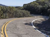 a motorcycle going down a winding hill road next to trees and a blue sky in the background